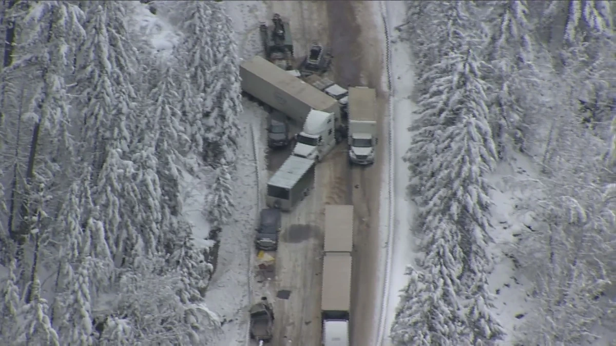 A semi-truck and passenger car collision on a snow-covered stretch of the Coquihalla Highway in British Columbia, showing the hazardous winter conditions where lane lines are obscured.